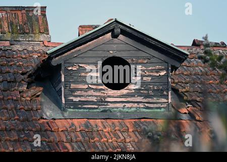An old house roof with chipped paint and a round window with the sunlight shining on it Stock Photo