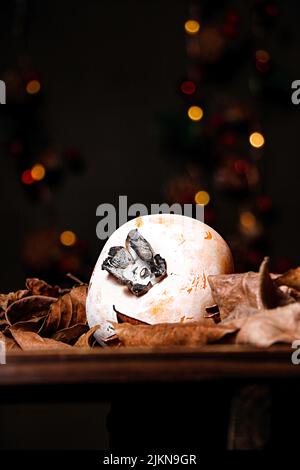 A vertical shot of a persimmon fruit on a table with dried leaves and bokeh lights in the background Stock Photo