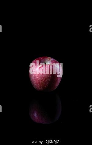 A vertical closeup of a red apple isolated on a black background with a reflection Stock Photo