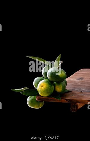 The vertical shot of green tangerines on a wooden table isolated on a black background Stock Photo
