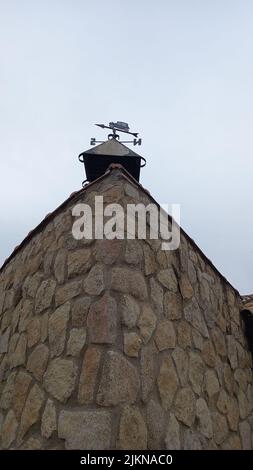A vertical shot of a  weather vane in the form of a car on the roof of an old stone house against a cloudy sky Stock Photo