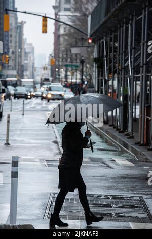 A vertical shot of a woman with an umbrella crossing the street on a rainy day Stock Photo