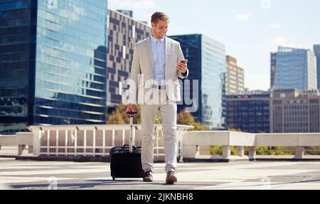 Getting work done on the go. a young businessman using a cellphone while walking with a suitcase in the city. Stock Photo