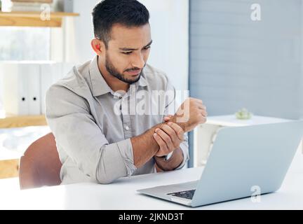 Listen to your body. a young man having pain in his wrist at work in a modern office. Stock Photo