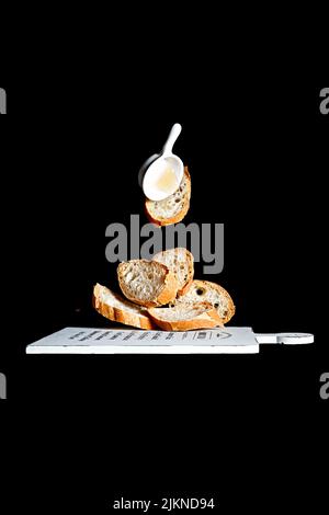 A vertical shot of tasty just baked baguette slices and sauce floating over a wooden cutting board Stock Photo