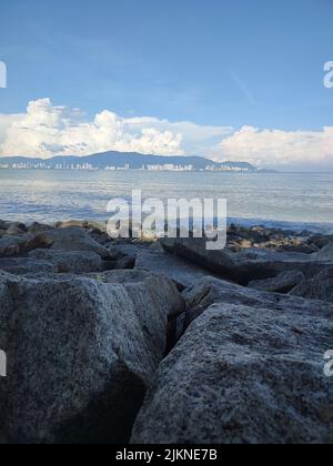 The rocks on the beach at Robina park with mountains on the horizon against blue cloudy sky on a sunny day. Penang, Malaysia Stock Photo