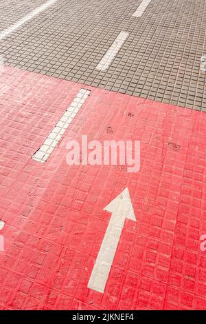 A vertical photo of an arrow sign on red cycle path Stock Photo