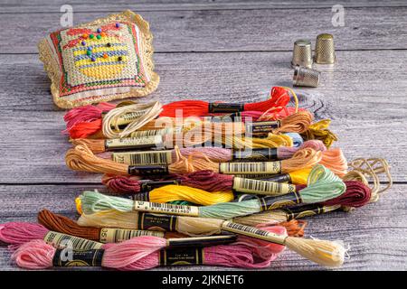A photo of colorful embroidery threads, a pin pillow and thimbles on a wooden table Stock Photo