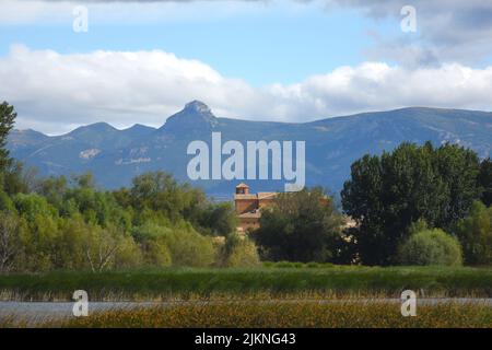 A landscape view of trees and a small brown building in the background of mountains and a cloudy sky Stock Photo