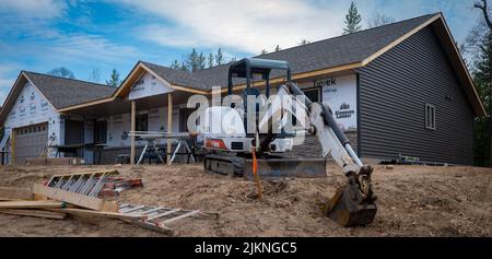 CROW WING CO, MN - 5 MAY 2022: Bobcat mini excavator with skid steer tracks, and ladders sit on dirt in front of a new home construction job site. Stock Photo