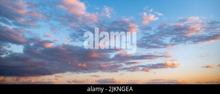 Evening blue sky and gray clouds with orange and pink highlights reflecting setting or rising sun, at dusk or dawn. Stock Photo
