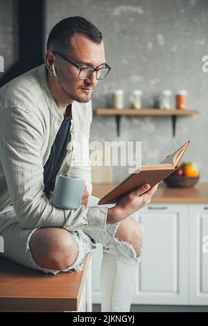 Man drinking coffee in the morning, making notes in paper notebook. Kitchen interior. For lifestyle design. Stock Photo