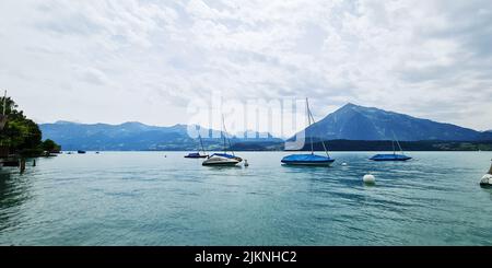 A bright summer day at a beach with small sailboats in the water surrounded by big mountains Stock Photo