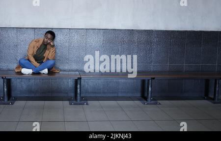 Shes thinking about running away. Full length shot of a young woman looking depressed while sitting on a bench in a train station terminal. Stock Photo