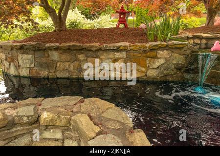 A small waterfall dropping in a river with red and green trees in the back in a beautiful park Stock Photo