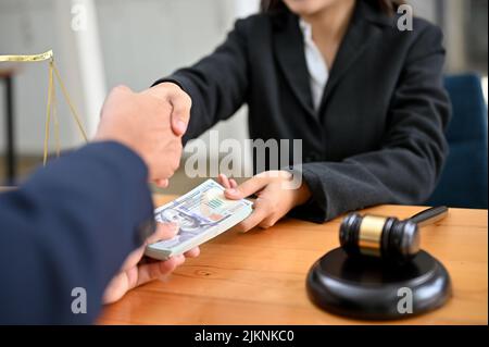 An Asian female lawyer or business legal consultant at the office desk receives money and shaking hand with her male client. cropped image Stock Photo