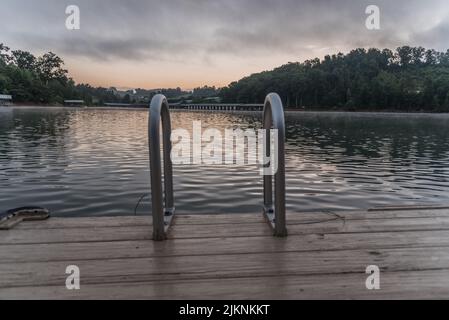 A beautiful view of a calm lake with a wooden swimming pier and metal ladders Stock Photo