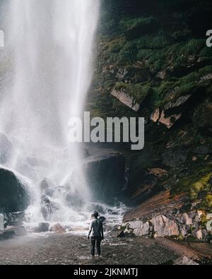 A man standing in front of a beautiful waterfall surrounded cliffs Stock Photo