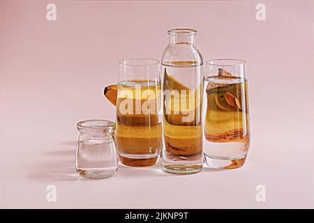 A transparent bottle of water and three glasses with bananas behind them on a pink background Stock Photo