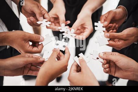 Putting together the missing links. Closeup shot of a group of unrecognisable businesspeople joining puzzle pieces together. Stock Photo