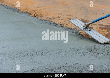 Mason worker is holding steel trowel and smoothing plastering new sidewalk on wet freshly poured concrete Stock Photo