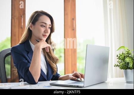 Charming and professional young Asian businesswoman or female executive manager focused working in her project on laptop computer. Stock Photo