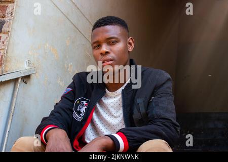 A black man in casual clothes sitting on the stairs and looking at camera Stock Photo