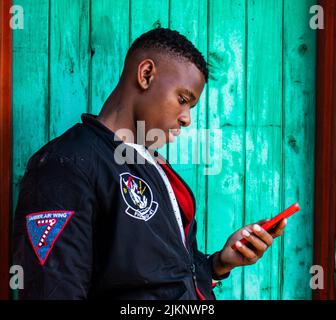A side view of black man in casual clothes on a blue wall background with phone in his hands Stock Photo