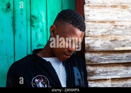 A black man in casual clothes on a blue wall background looking down Stock Photo