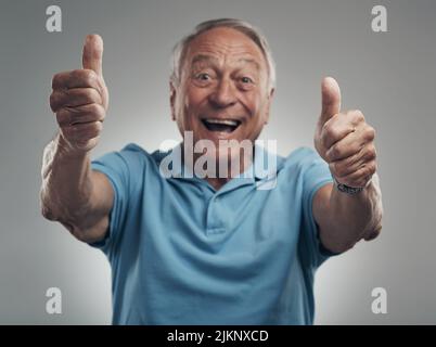 We should definitely do that again. a happy elderly man giving the thumbs up in a studio against a grey background. Stock Photo
