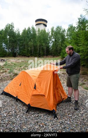 Germany. 15th July, 2022. ILLUSTRATION - A man pitching his tent on the trekking site Frankenwald Thüringer Warte. The Thüringer Warte lookout tower can be seen in the background. In the Franconian Forest and the Bavarian Forest, you can camp in some places away from regular campsites. (to dpa Trekking instead of wild camping: Camping in Bavaria's nature) Credit: Nicolas Armer/dpa/Alamy Live News Stock Photo