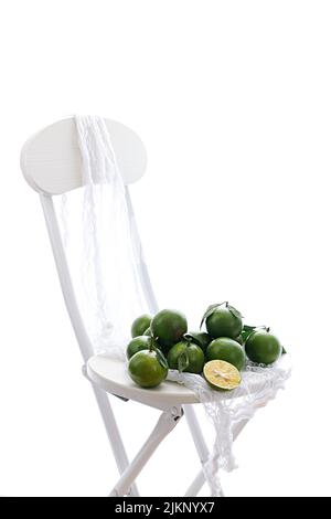 A vertical shot of bunch of green limes on white chair isolated on white background Stock Photo