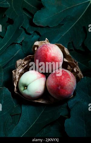 A vertical shot of peaches in brown paper in background of leaves Stock Photo