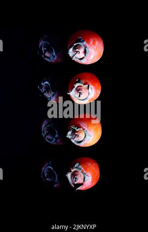 A vertical shot of ripe Persimmons isolated on a black background Stock Photo