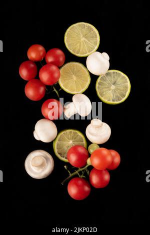 A vertical shot of tomatoes, lemons, and mushrooms isolated on the black background Stock Photo