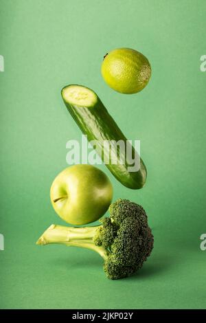 A vertical shot of floating healthy vegetables and apple isolated on green background Stock Photo