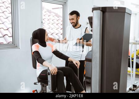 Personal trainer helping woman working with leg weight machine at the gym Stock Photo