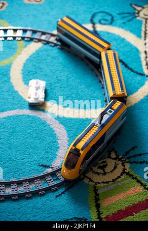 a vertical shot of a Lego brand toy model train with track on a carpet floor. Stock Photo