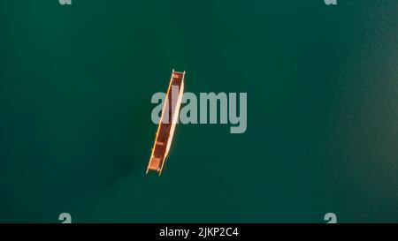 A vertical aerial shot of a small wooden boat on a green body of water Stock Photo