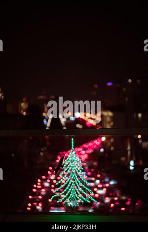 A beautiful shot of a green Christmas lights tree with blurred bokeh lights in the background at night Stock Photo