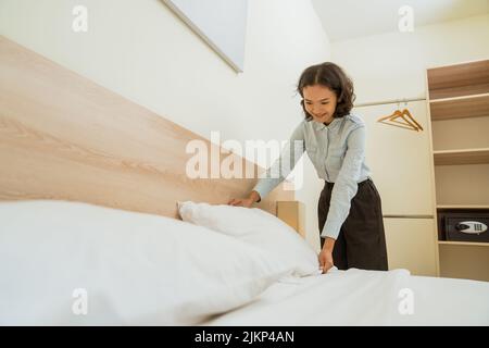 Asian female cleaning staff tidying pillows on bed Stock Photo