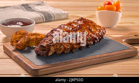 A closeup shot of a tasty grilled pork ribs with fried onion rings sauce and cherry tomatoes on a wooden table Stock Photo