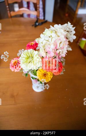 A bouquet of colorful flowers sits on a table in a white vase indo Stock Photo