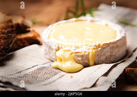 A closeup shot of baked camembert cheese on a cloth with sliced brown bread Stock Photo