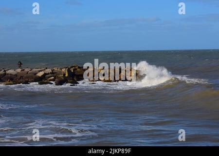 A Beautiful shot of a wavy sea crashing stones in a beach under a blue sky on a sunny day Stock Photo