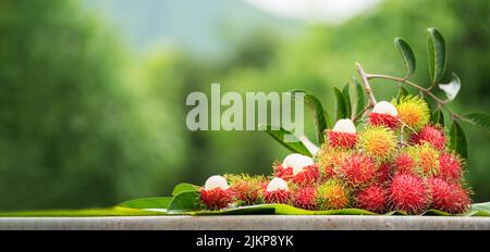 The Pile of Rambutan sweet delicious fruit with Leaf on green jungles tree of rambutan soft focus background, Peel half of the rambutan fruit Stock Photo