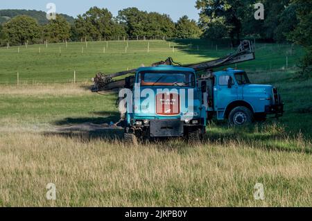 Two old blue trucks with crane abandoned in the field Stock Photo