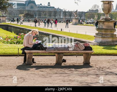 A couple on a bench in the beautiful Tuileries garden in Paris, the man is sleeping and his wife is writing Stock Photo
