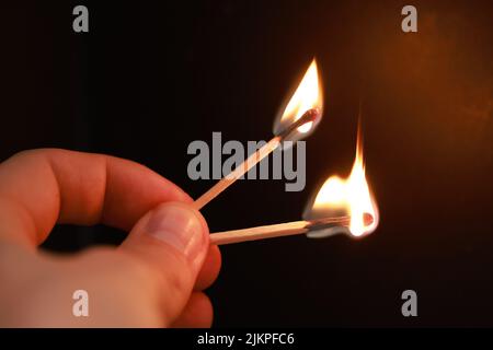A closeup of a hand holding two burning match sticks on a black background with copyspace Stock Photo