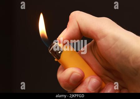 A closeup of a hand holding a burning cigarette lighter on a black blurry background with copyspace Stock Photo